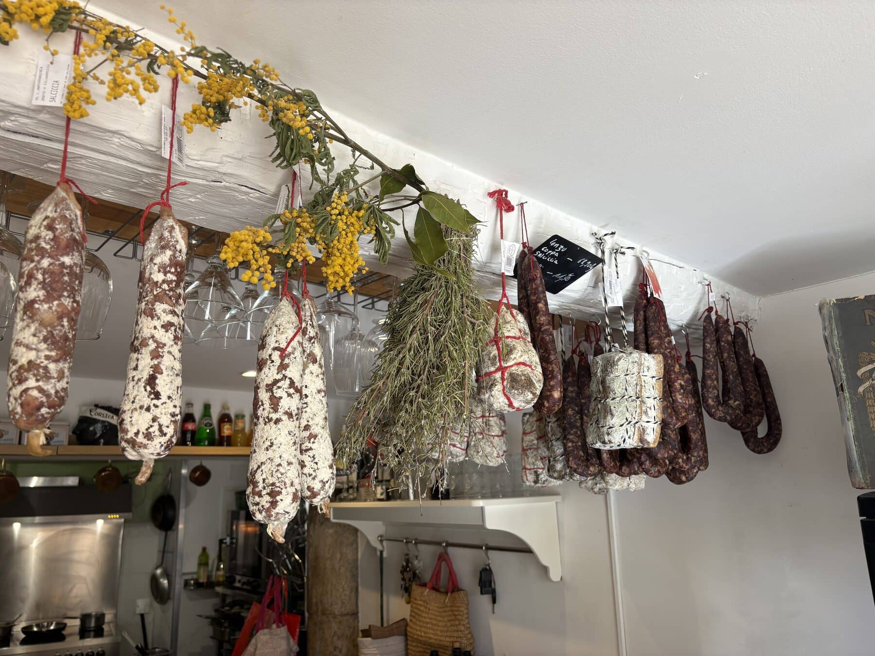Charcuteries corses suspendues au plafond de l’épicerie, mêlées à des bouquets de fleurs séchées.