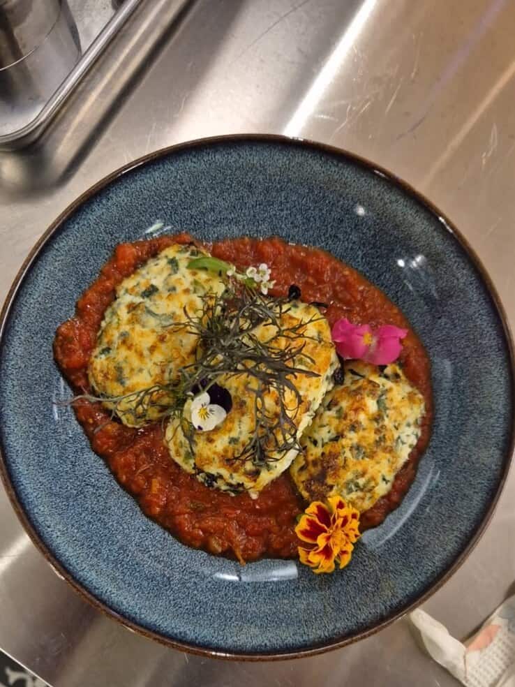 Storzapretti : quenelles de brocciu gratinées à la tomme de brebis, sur une sauce tomate aux herbes du maquis, dans un bol bleu.