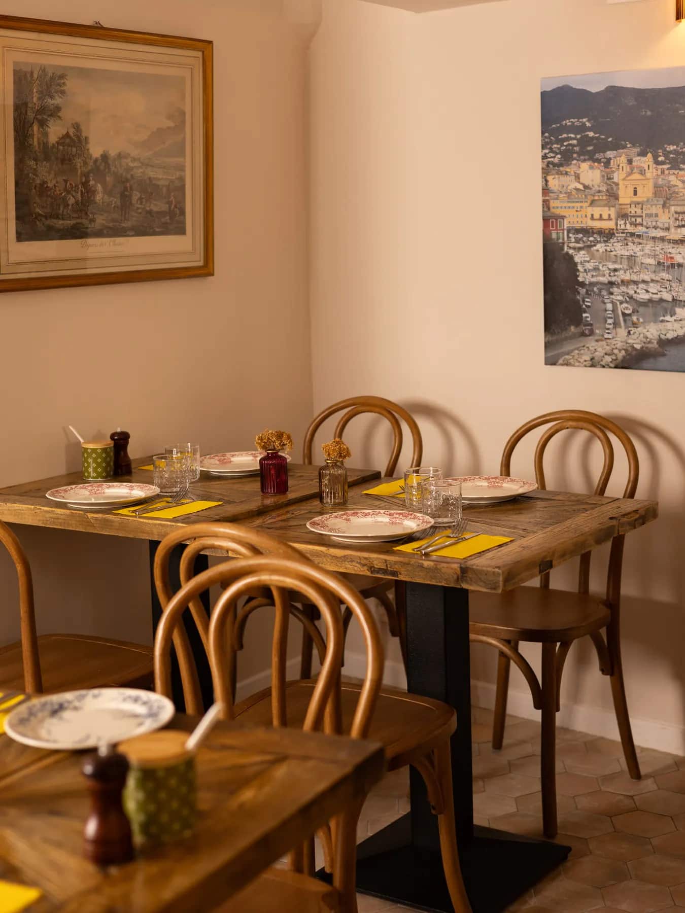 La salle du bistrot : table dressée, chaises en bois courbé et murs couverts de cadres anciens.