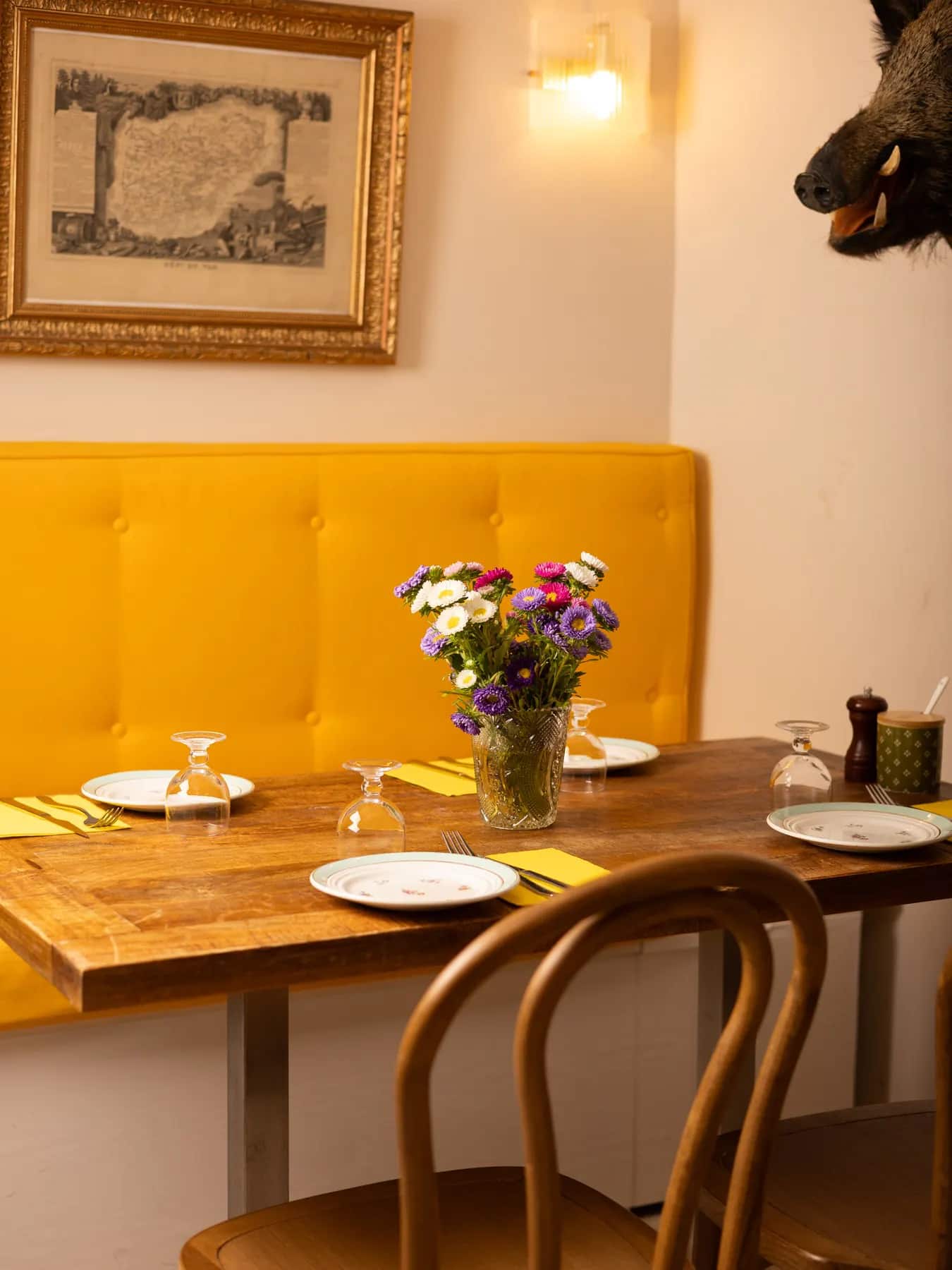 Table dressée devant la banquette jaune, verres à pied et fleurs fraîches.
