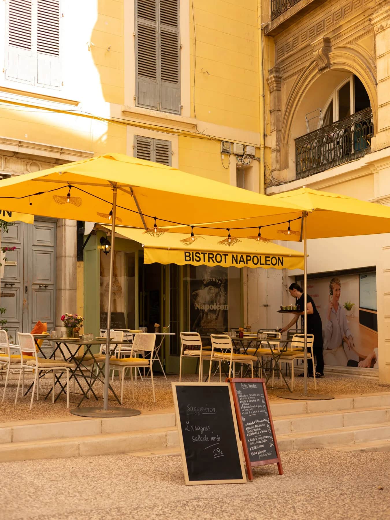 La façade jaune du Bistrot Napoléon, avenue des Îles d’Or à Hyères, sa marquise et ses parasols jaunes.